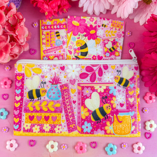 A colorful pouch with bee designs on a pink background with flowers